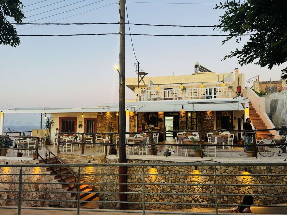 A wide frontal view of the taverna at dusk from the lane.