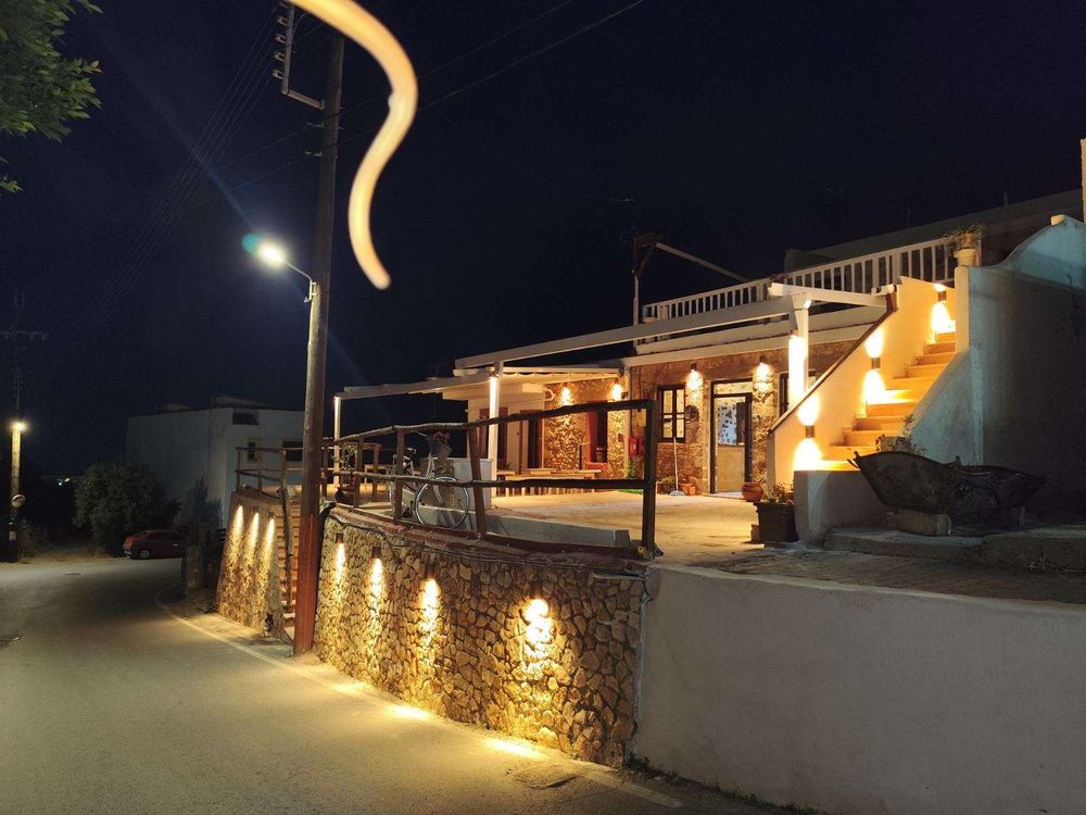 The street at night, a lit stone wall running alongside the taverna.