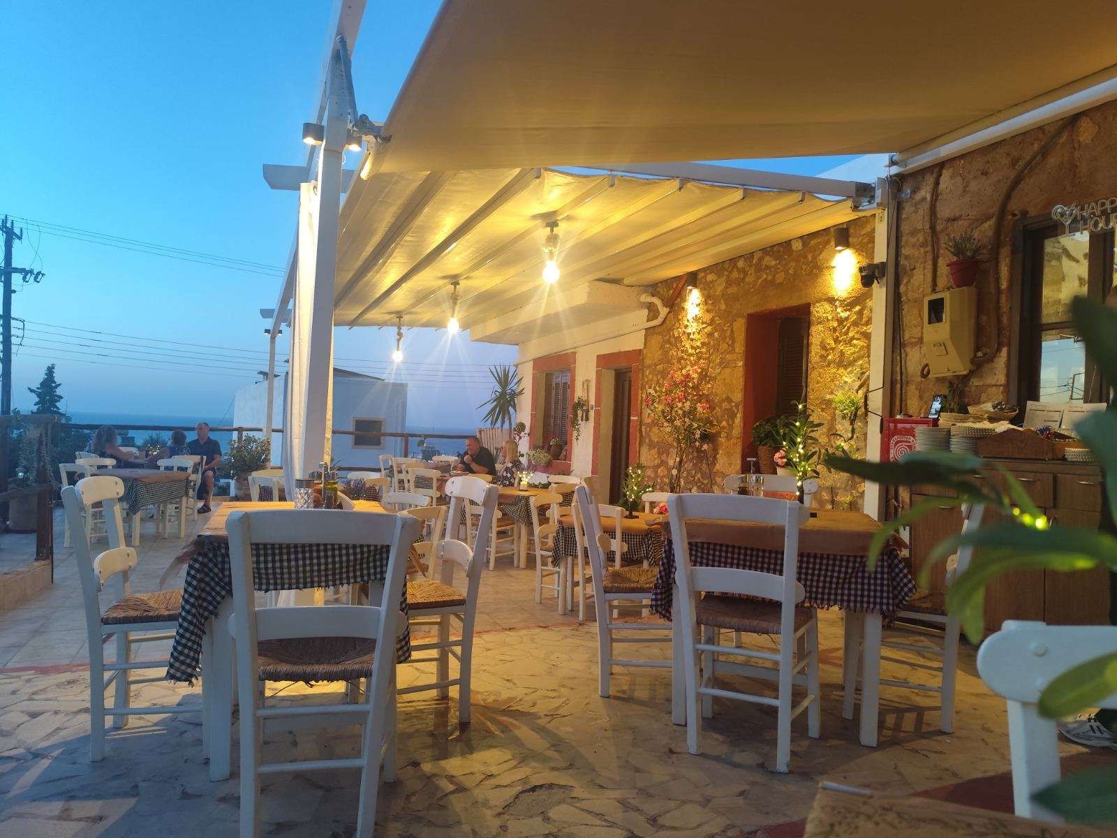 The terrace at dusk, string lights glowing over set tables, the darkening sea beyond.