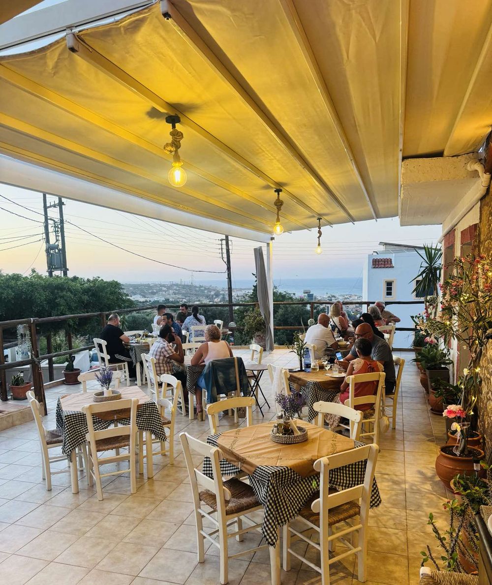 The full terrace at golden hour, guests at every table, the sea below.
